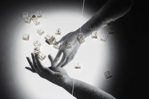 Deux ombres de mains tendues se rejoignent au centre d’un cercle lumineux. Des petits cubes blancs illustrés flottent autour, projetant des effets visuels qui donnent une impression de mouvement suspendu.